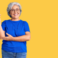 Senior woman pointing up on yellow background