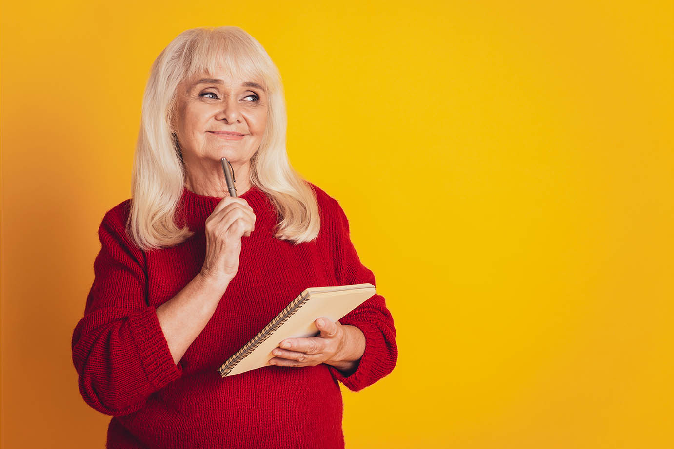 Senior woman with a pen and notepad on a yellow background