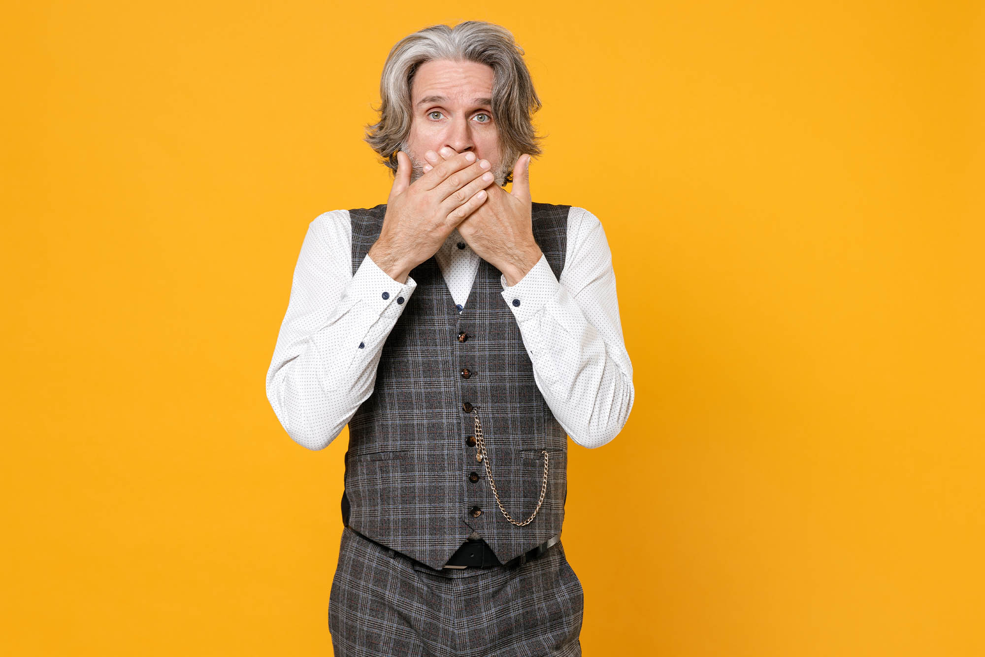 Senior gentleman with hands over mouth on yellow background