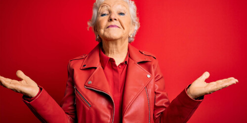 Senior woman shrugging while looking at the camera on red background