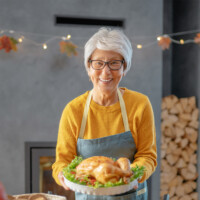 Phone conversation. Positive senior aged woman smiling while offering a roasted chicken