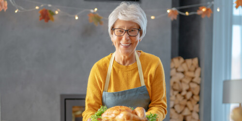 Phone conversation. Positive senior aged woman smiling while offering a roasted chicken